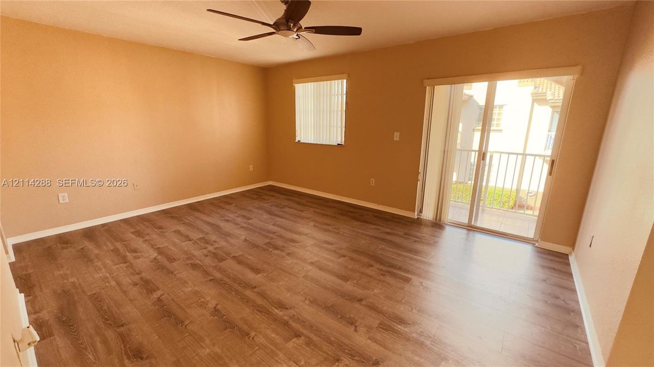 Spacious room featuring wood-finish flooring, a ceiling fan, a window with vertical blinds, and a sliding glass door providing external access