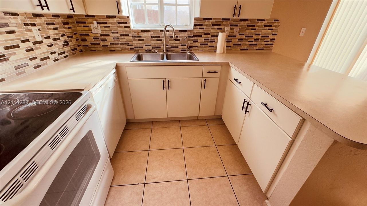 Kitchen featuring white cabinetry, solid-surface countertops, mosaic tile backsplash, dual-basin stainless steel sink, and ceramic tile flooring