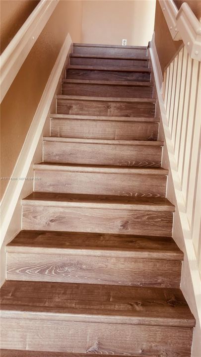 Staircase featuring wood-finish treads, white vertical balusters, and a matching handrail