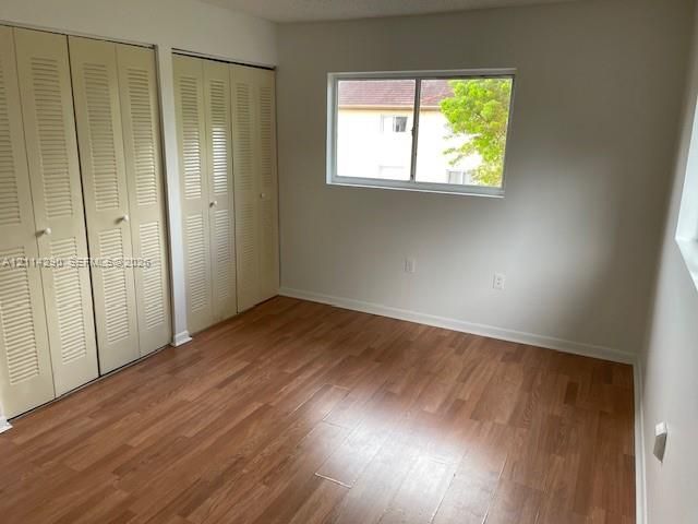 Room featuring wood-finish flooring, dual sets of bi-fold louvered closet doors, and a horizontal sliding window