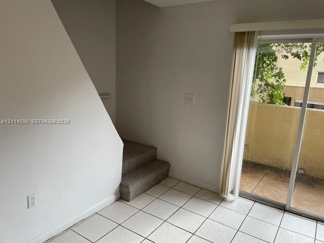 Interior space featuring white tile flooring, carpeted stairs, and a sliding glass door with vertical blinds