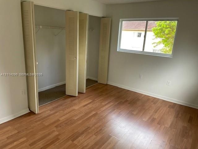 Room featuring wood-finish flooring, a horizontal sliding window, and a dual-panel louvered closet with an integrated clothing rod