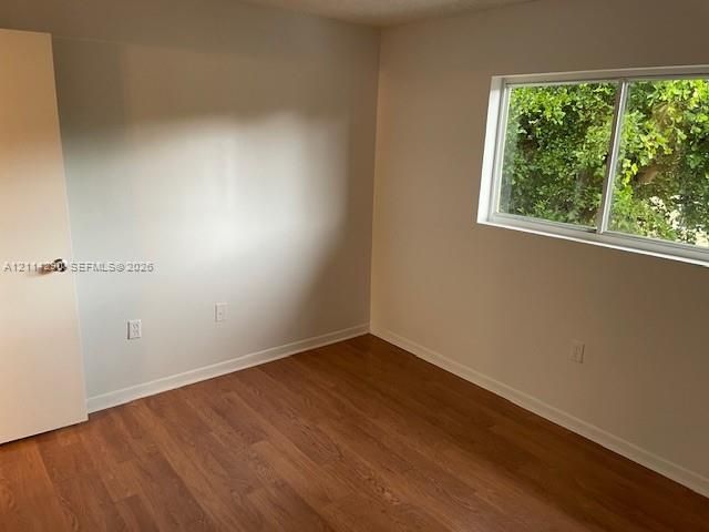 Room featuring wood-finish flooring, neutral wall paint, and a sliding window with exterior foliage