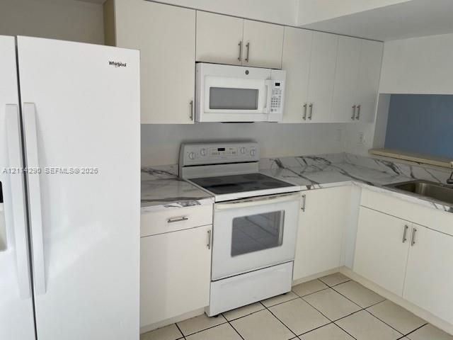 Kitchen featuring white cabinetry, stone-patterned countertops, a stainless steel sink, and integrated white appliances including a refrigerator, electric range, and over-the-range microwave
