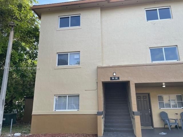 Multi-story exterior featuring a textured stucco finish, two-tone earth-tone color scheme, sliding windows, and a covered entryway with built-in exterior lighting