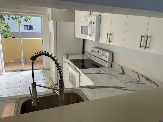 Kitchen featuring white flat-panel cabinetry, stone-patterned countertops, a stainless steel industrial-style pull-down faucet, a built-in microwave, and tile flooring