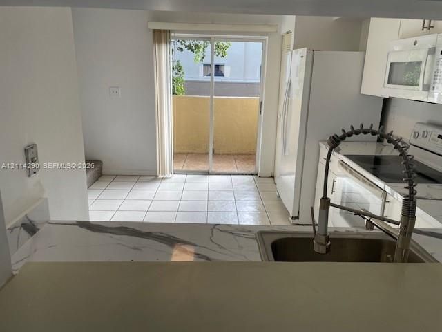Kitchen featuring white cabinetry, an under-mount sink with a high-arch spring faucet, stone-finish countertops, tiled flooring, and sliding glass doors