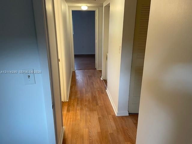 Hallway featuring wood-finish flooring, neutral wall tones, and louvered-panel closet doors