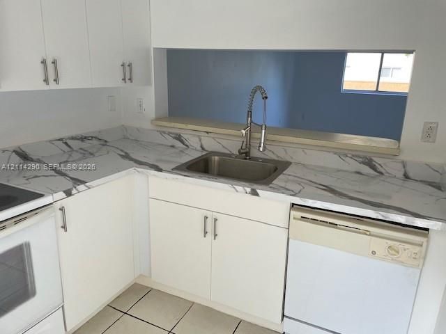 Kitchen featuring white cabinetry with metallic pulls, stone-patterned countertops, stainless steel undermount sink, gooseneck faucet, and tile flooring