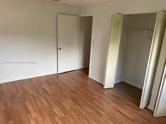 Room featuring wood-finish flooring, neutral wall paint, and a built-in closet with folding doors