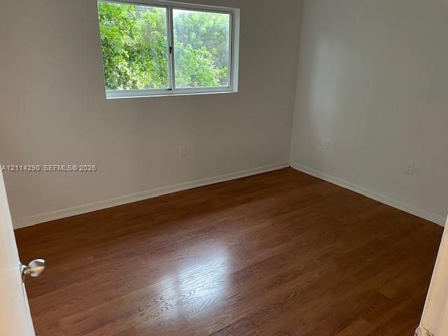 Room featuring wood-finish flooring, neutral wall paint, and a sliding window with exterior foliage