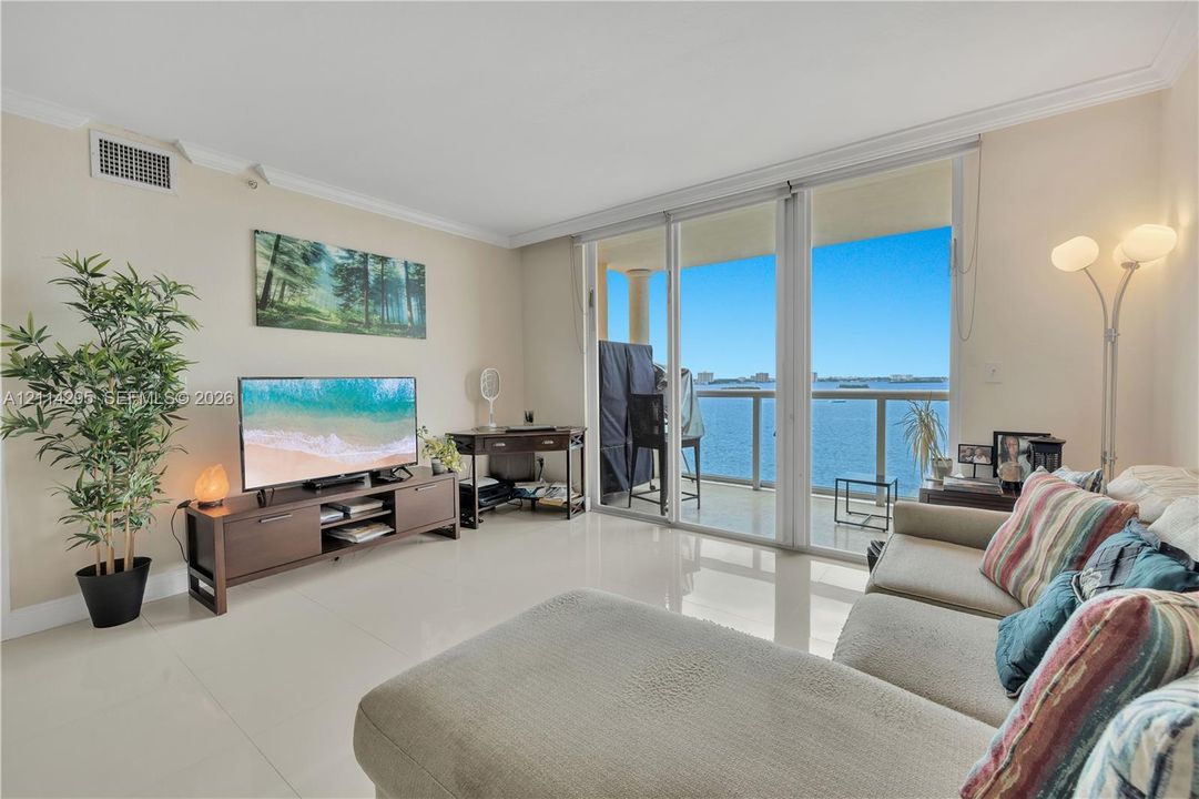 Living area featuring large-format tile flooring, floor-to-ceiling glass sliding doors, and a private balcony with metal railing