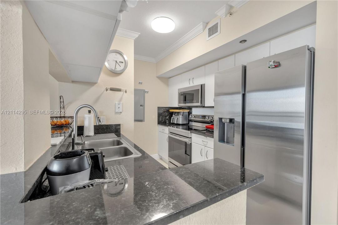 Kitchen featuring dark stone countertops, stainless steel appliances, white cabinetry, a dual-basin undermount sink, and crown molding