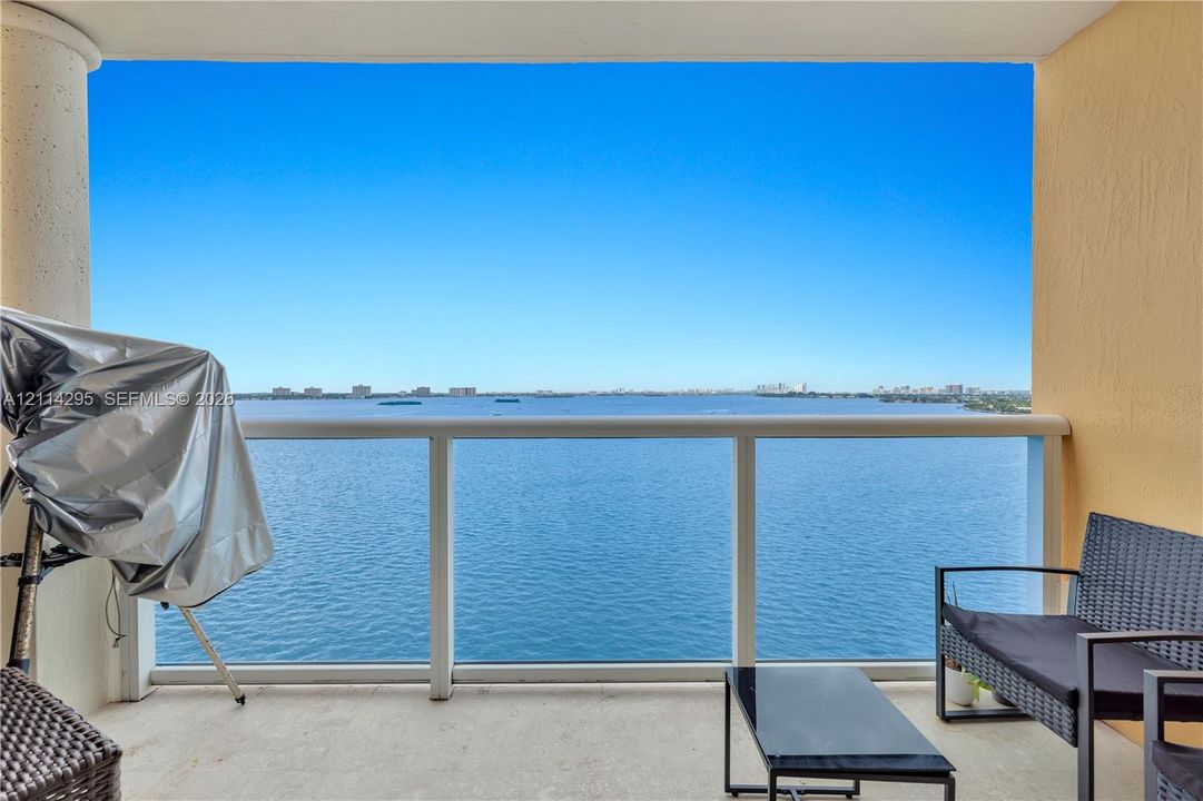 Covered balcony featuring a concrete floor, structural column, and white metal railing with glass panels overlooking the water