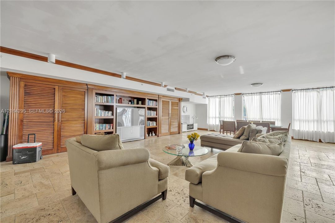 Extensive built-in wood cabinetry with integrated shelving, stone tile flooring, and floor-to-ceiling windows with neutral drapery