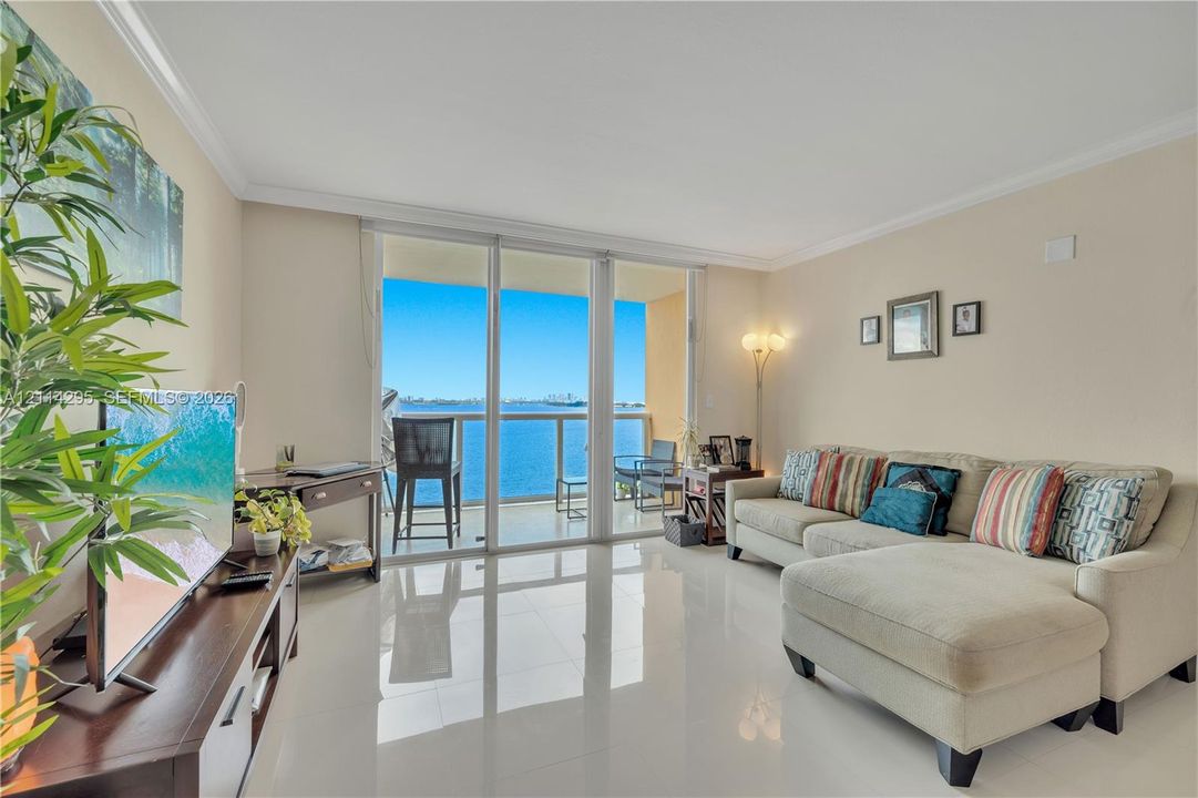Living area featuring large-format tile flooring, crown molding, and floor-to-ceiling glass doors opening to a private balcony