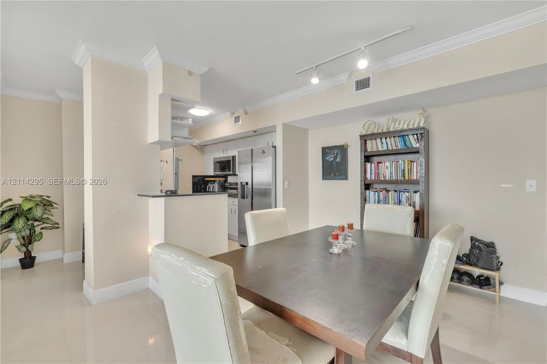Open kitchen featuring stainless steel appliances, crisp white cabinetry, and crown molding, accented by overhead track lighting and neutral tile flooring
