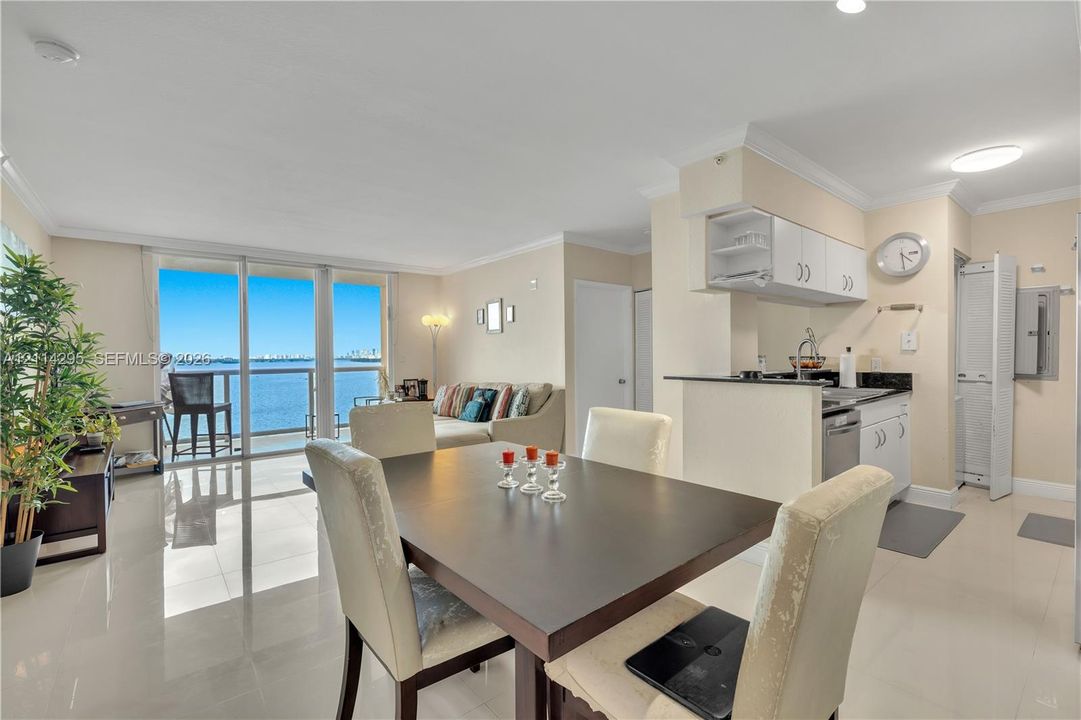 Open-concept living space featuring high-gloss tile flooring, floor-to-ceiling glass doors, and a kitchen equipped with white cabinetry, stone-surfaced countertops, and a stainless steel dishwasher
