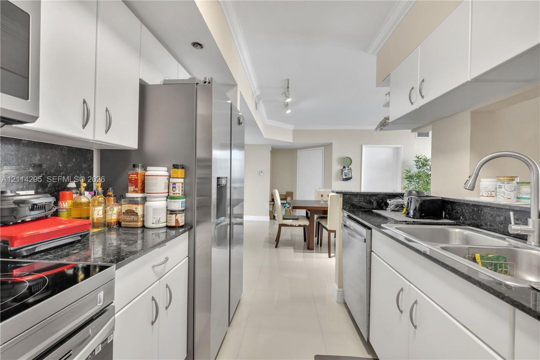 Kitchen featuring white cabinetry, stone-finish countertops, stainless steel appliances, a double-basin undermount sink, and tile flooring