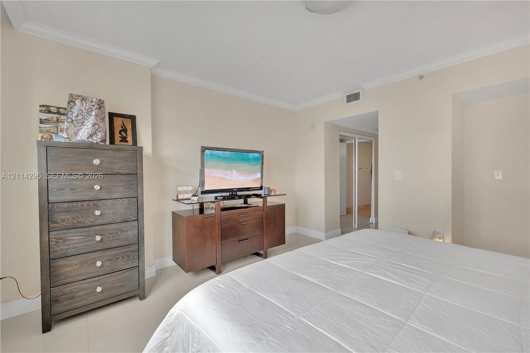 Neutral-toned interior space featuring light tile flooring, crown molding, and a closet with mirrored sliding doors