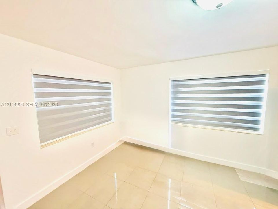 Neutral-toned tile flooring, white wall finishes, and dual windows equipped with horizontal zebra-style roller shades
