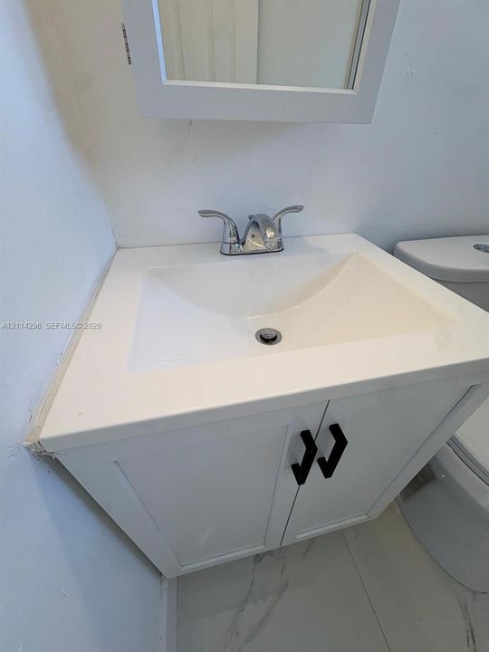 White vanity featuring a rectangular integrated sink, chrome double-handle faucet, matte black hardware, and large-format tile flooring