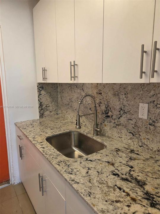 Flat-panel cabinetry with brushed nickel hardware, stone countertops, matching stone backsplash, under-mount stainless steel sink, and a high-arch gooseneck faucet