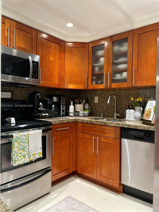 Kitchen featuring shaker-style wood cabinetry with glass-front uppers, stainless steel appliances, stone countertops, and a stainless steel gooseneck faucet