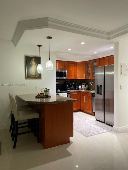 Kitchen featuring stained wood cabinetry, stone-surface countertops, stainless steel appliances, recessed ceiling lighting, and dual pendant light fixtures