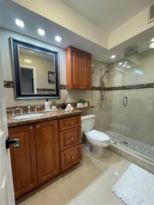 Bathroom featuring natural wood-finish cabinetry, stone countertop with integrated sink, recessed lighting, and a glass-enclosed shower with tiled flooring and a wall-mounted shower fixture
