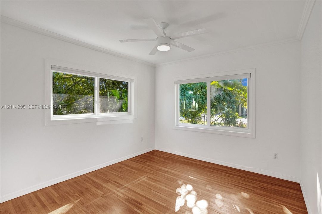 Room featuring wood-finish flooring, dual windows, crown molding, and a central ceiling fan with integrated lighting