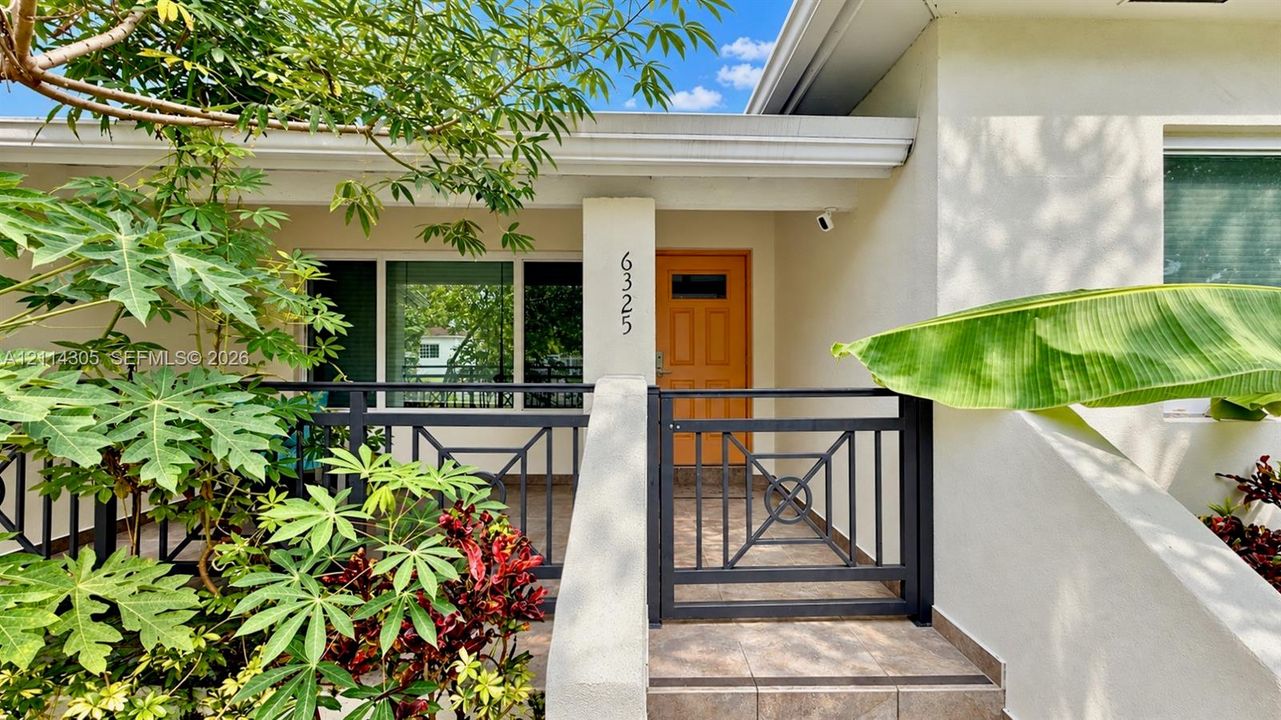 Exterior entry featuring a covered patio with tiled flooring, a decorative metal gate, and stucco wall finishes