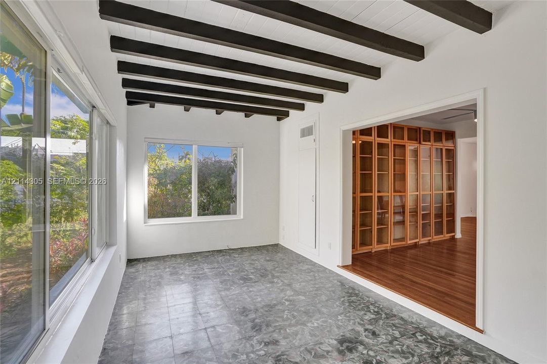 Exposed dark wood ceiling beams, stone tile flooring, large multi-pane windows, and built-in floor-to-ceiling wood cabinetry