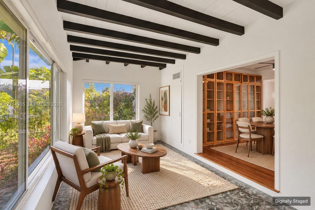 Sunroom featuring exposed dark wood ceiling beams, floor-to-ceiling windows, and patterned stone flooring, with built-in wood-framed glass cabinetry