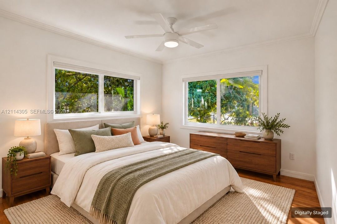 Neutral-toned interior featuring hardwood flooring, crown molding, a central ceiling fan with integrated lighting, and multiple sliding windows