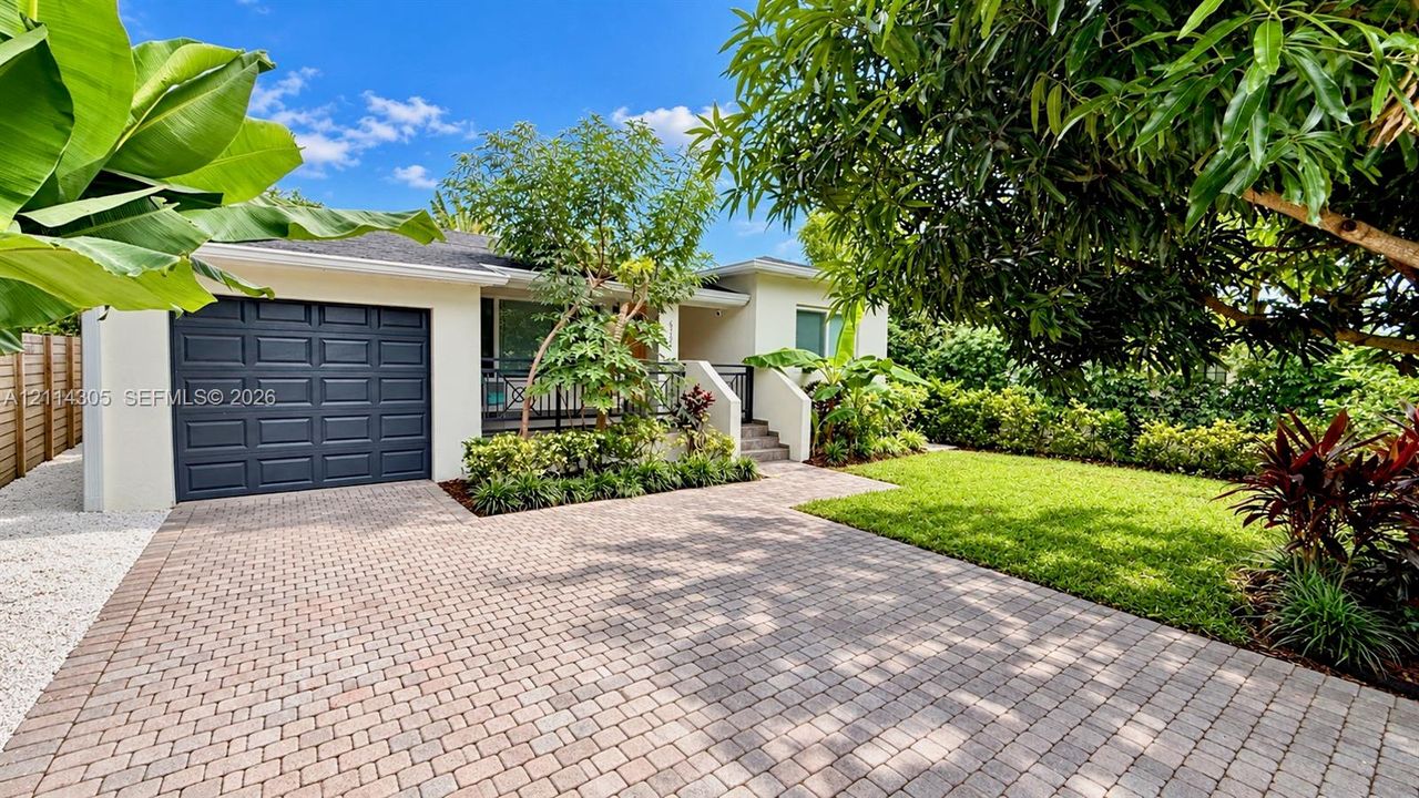 Stucco exterior featuring a paver driveway, single-car garage, manicured lawn, and mature landscaping