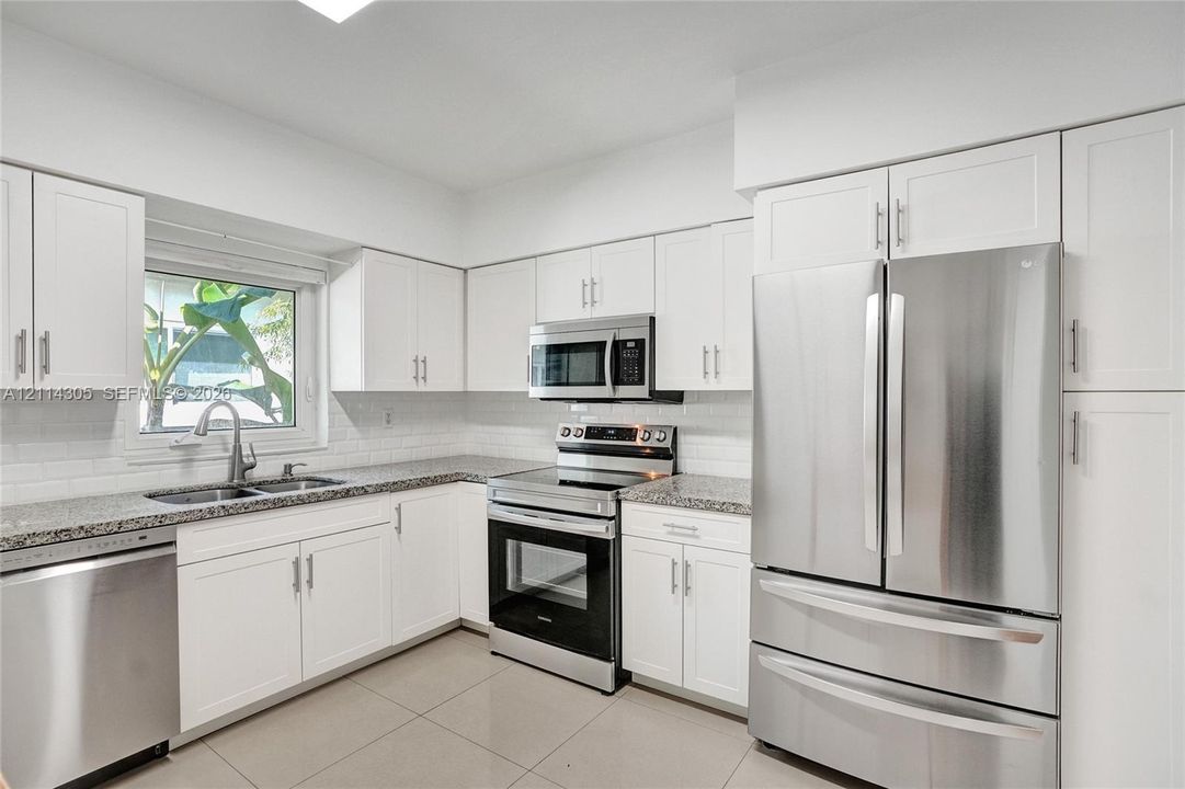 Kitchen featuring white shaker-style cabinetry, stone-finish countertops, subway tile backsplash, stainless steel appliances, and large-format tile flooring