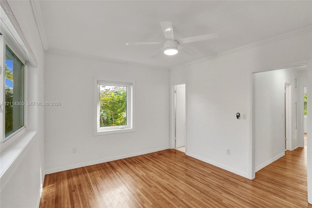 Room featuring wood-finish flooring, white walls, crown molding, double-pane windows, and a central ceiling fan with an integrated light fixture