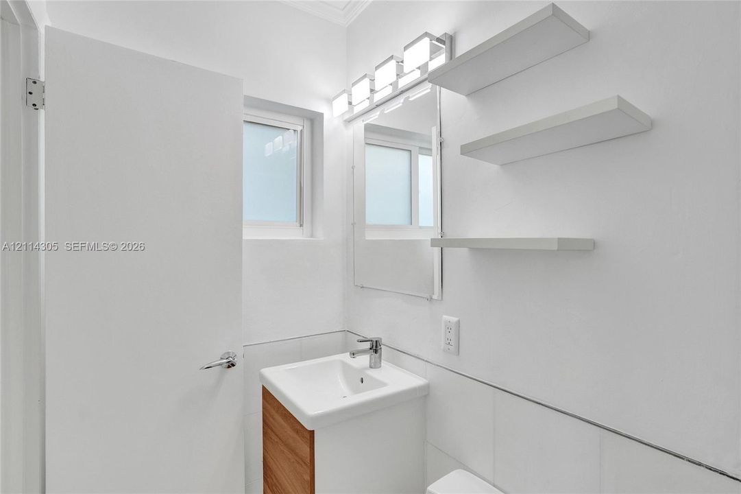 Wall-mounted vanity with wood-finish cabinetry, rectangular basin, chrome faucet, three floating wall shelves, and multi-bulb vanity light fixture