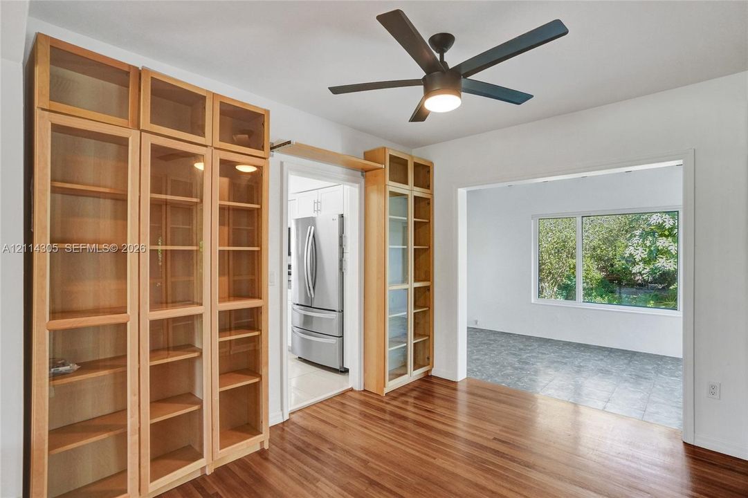 Built-in light-wood cabinetry with glass-front display doors, wood-finish flooring, and a modern ceiling fan with integrated lighting