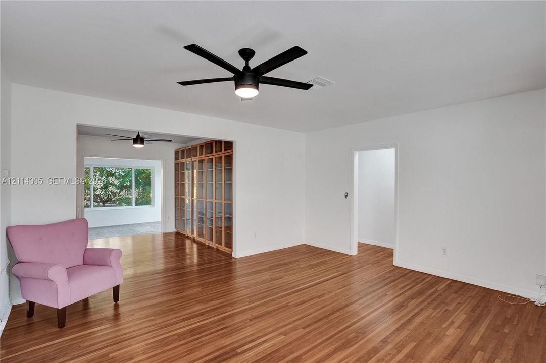 Living area featuring wood-finish flooring, a matte black multi-blade ceiling fan, and built-in floor-to-ceiling glass-paneled cabinetry