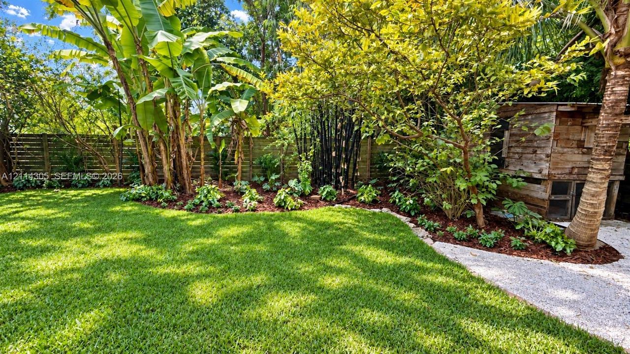 Landscaped backyard featuring a manicured lawn, horizontal slat wood fencing, tropical plantings, a gravel pathway, and a wood-structure garden shed
