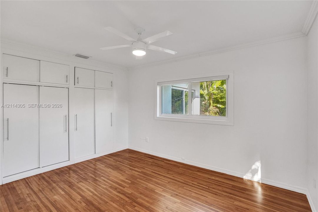 Room featuring wood-finish flooring, built-in floor-to-ceiling storage cabinetry with vertical hardware, a sliding window, and a ceiling fan with integrated lighting