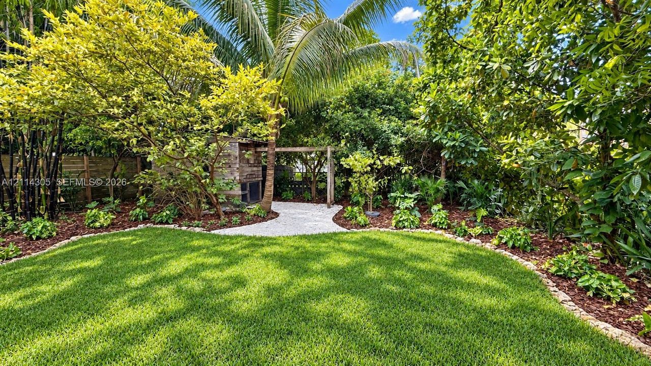 Backyard featuring a manicured lawn, stone-paved walkway, pergola, mature landscaping, and wood-slat perimeter fencing