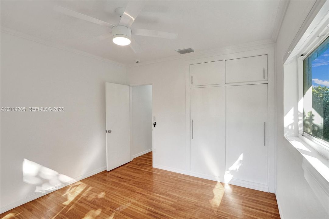 Wood-finish flooring, white built-in floor-to-ceiling cabinetry with vertical hardware, and a ceiling fan with integrated lighting