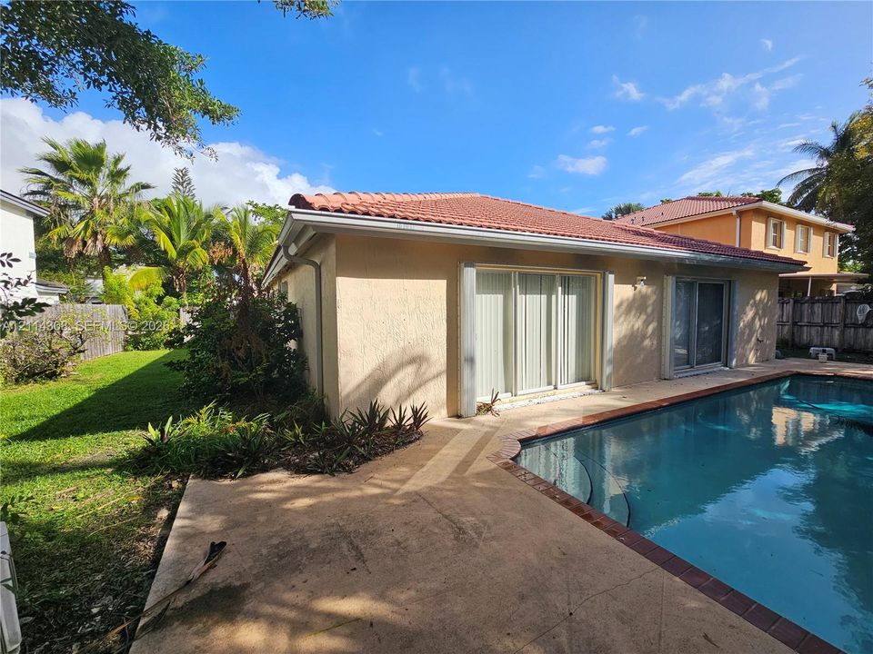 Rear exterior featuring a tile roof, concrete patio, swimming pool with perimeter edging, and sliding glass doors