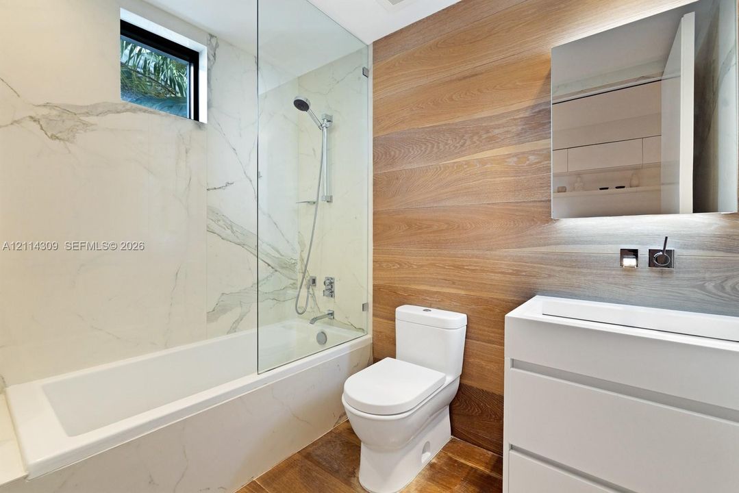 Bathroom featuring a wall-mounted vanity, wood-finish wall paneling, full-height tile surrounds, a frameless glass shower partition, and a wall-recessed medicine cabinet