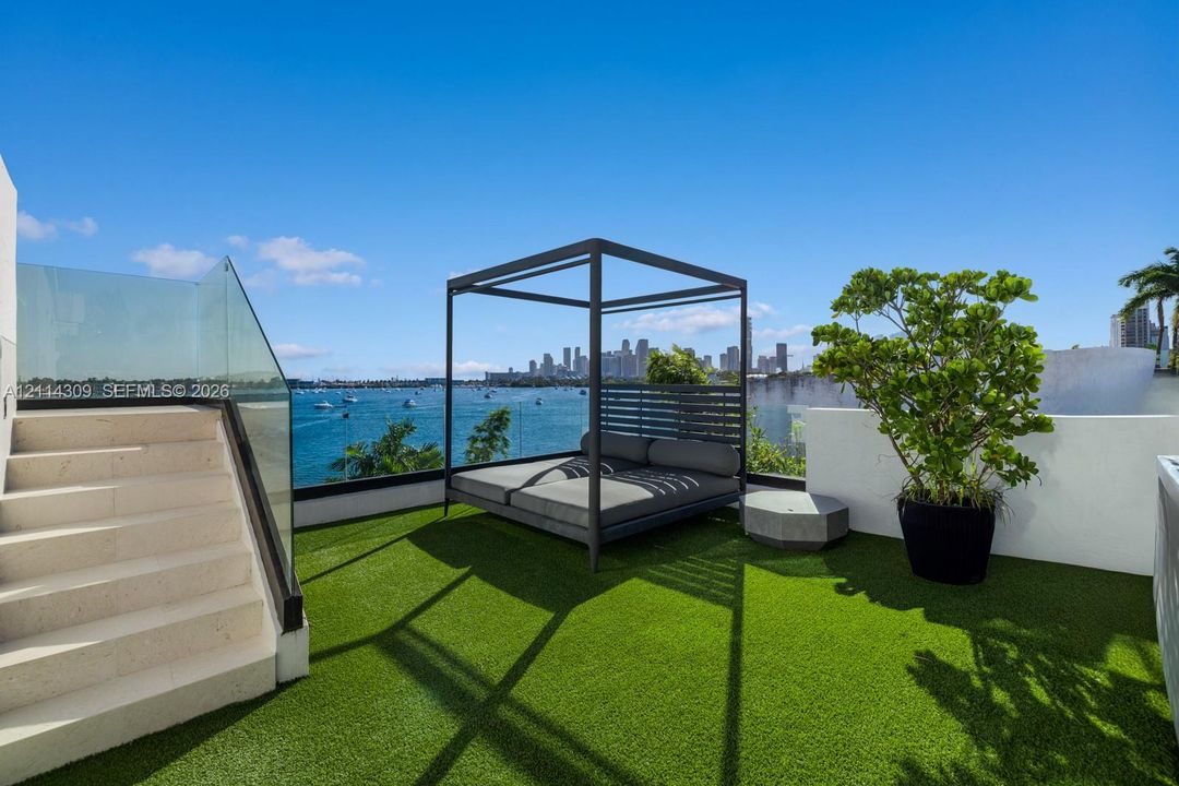 Rooftop terrace featuring synthetic turf flooring, glass panel railings, and light-toned stone stairs