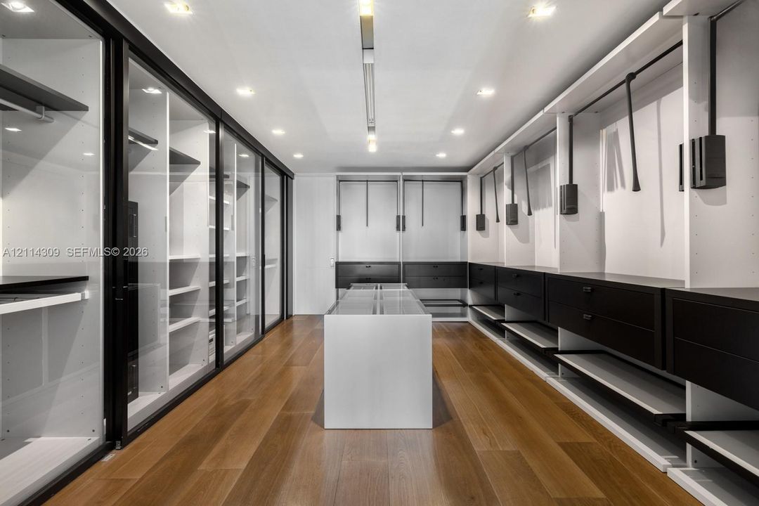Custom walk-in closet featuring glass-front cabinetry, a central storage island, recessed lighting, and wood-finish flooring