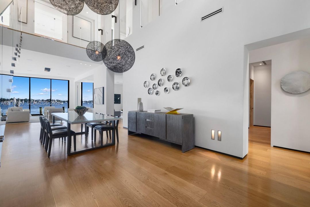 Double-height ceiling featuring oversized spherical pendant lighting, wide-plank wood-finish flooring, and expansive floor-to-ceiling windows